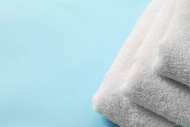 Photo of Stacked clean terry towels on light blue background, closeup. Space for text