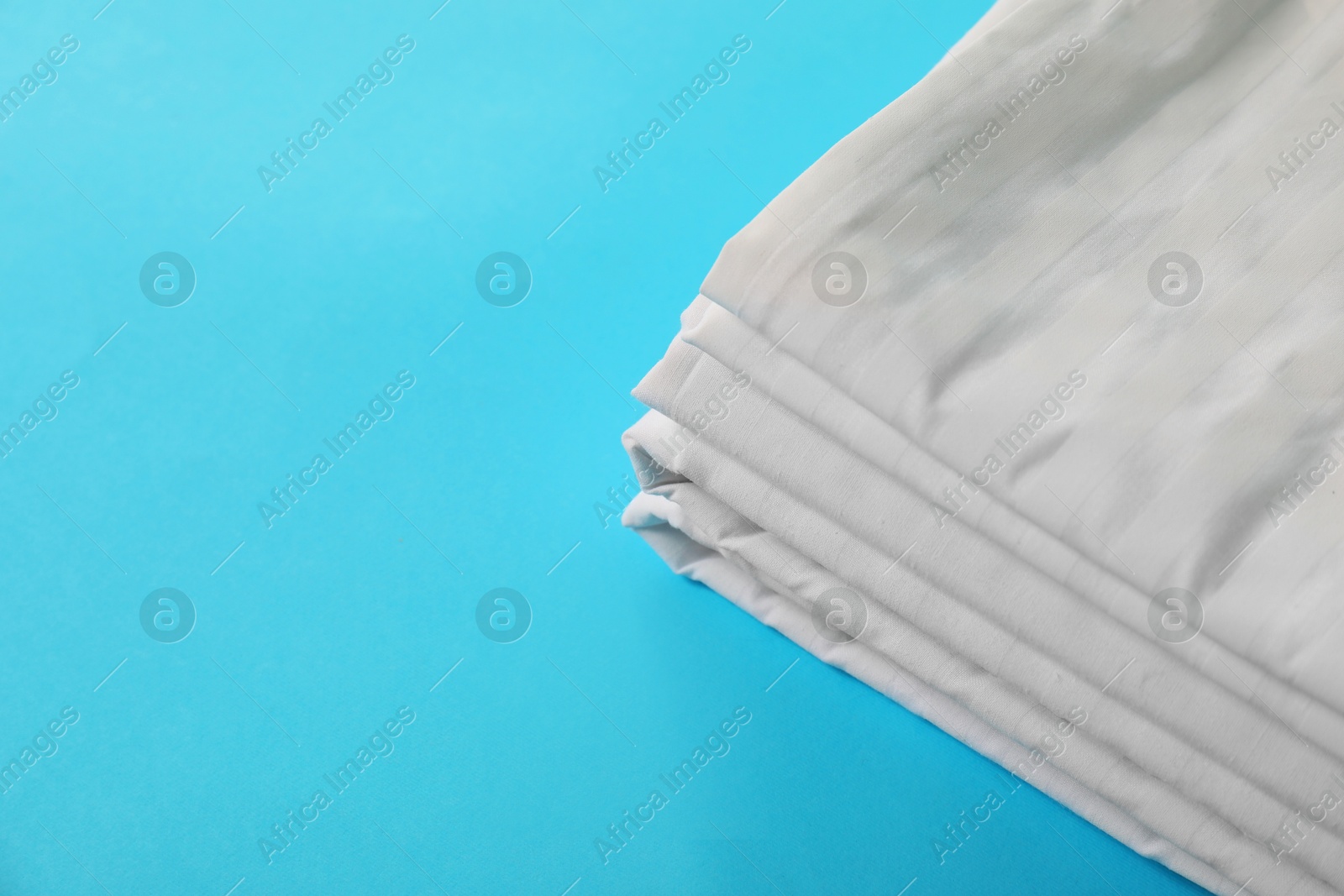 Photo of Stacked clean bed linens on light blue background, space for text