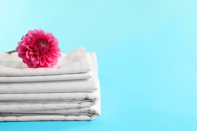 Photo of Stacked clean bed linens and pink flower on light blue background, space for text