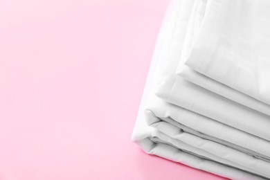 Photo of Stacked clean bed linens on pink background, closeup. Space for text