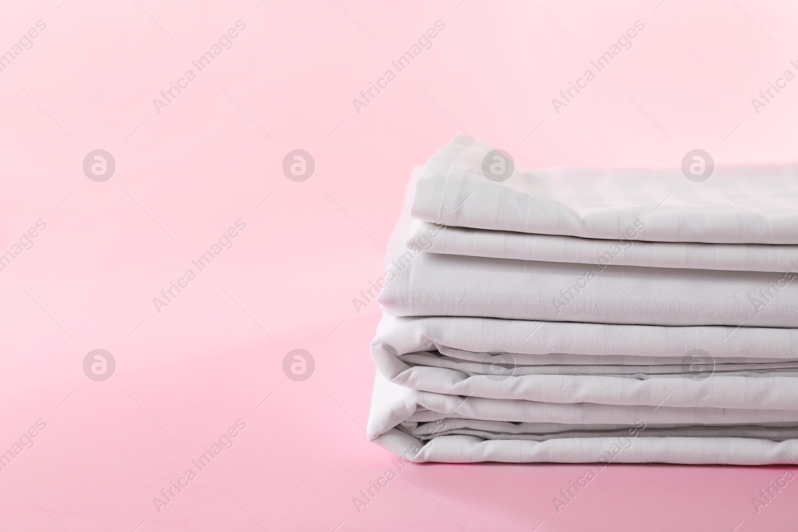 Photo of Stacked clean bed linens on pink background, space for text