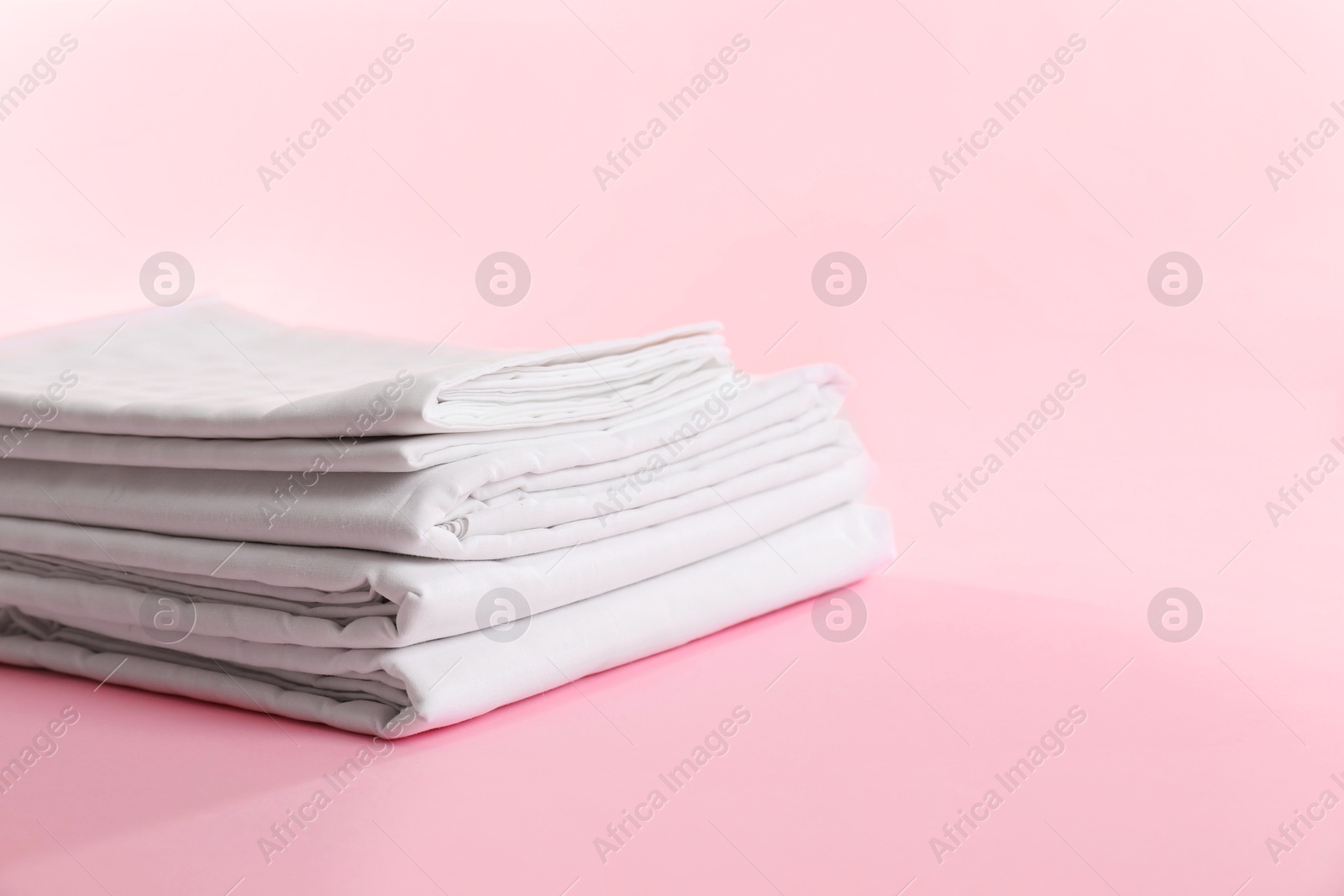 Photo of Stacked clean bed linens on pink background, space for text