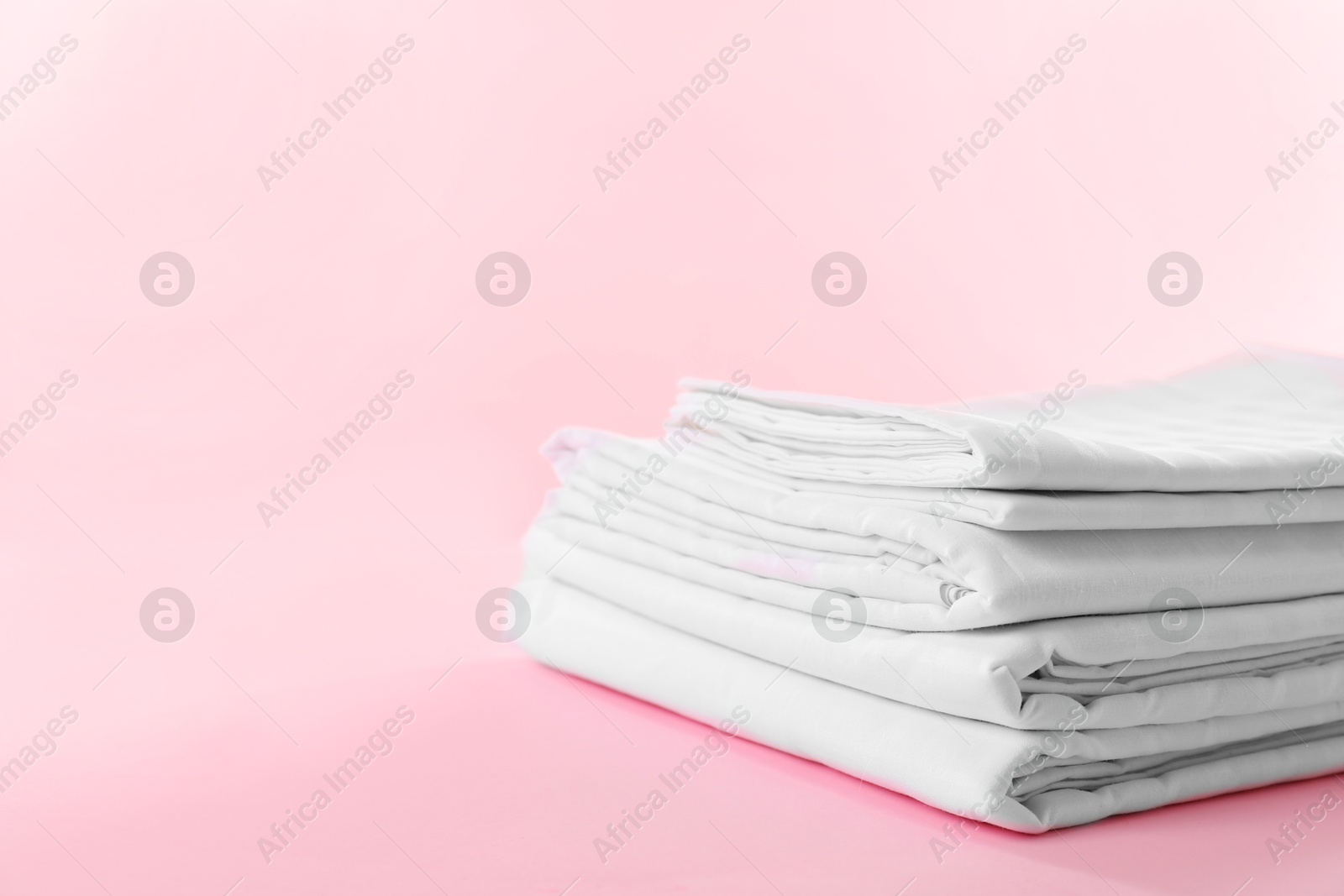 Photo of Stacked clean bed linens on pink background, space for text