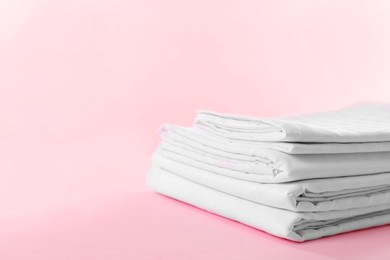 Photo of Stacked clean bed linens on pink background, space for text