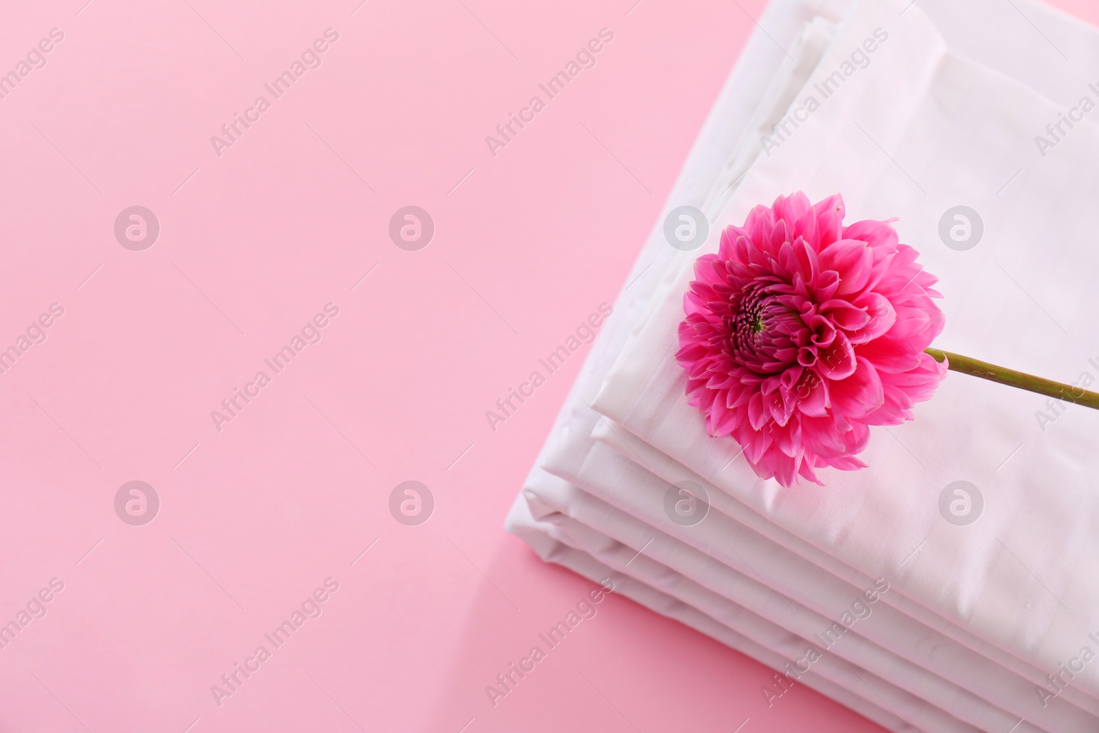 Photo of Stacked clean bed linens and flower on pink background, top view. Space for text