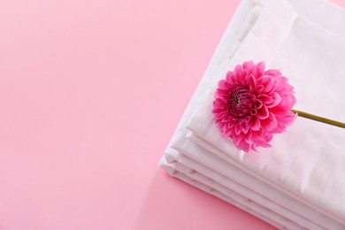 Photo of Stacked clean bed linens and flower on pink background, top view. Space for text