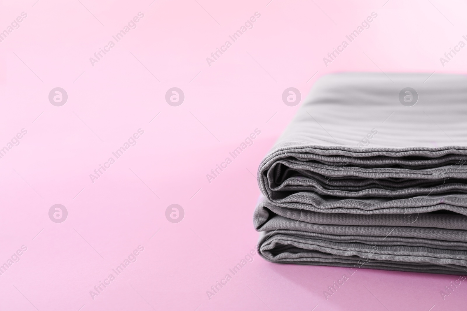 Photo of Stacked clean bed linens on pink background, closeup. Space for text