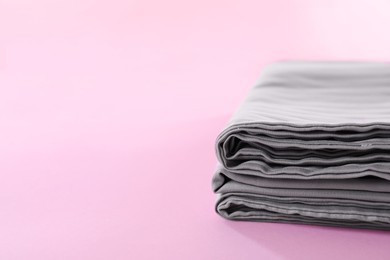 Photo of Stacked clean bed linens on pink background, closeup. Space for text