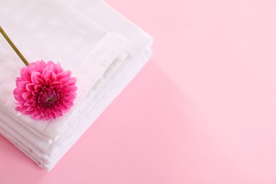 Photo of Stacked clean bed linens and flower on pink background, top view. Space for text