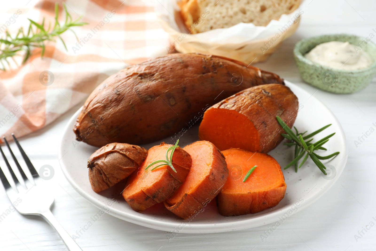 Photo of Tasty cooked sweet potatoes served with rosemary on white wooden table, closeup