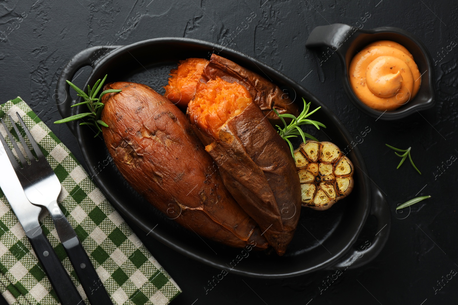 Photo of Tasty cooked sweet potatoes served with rosemary and sauce on black table, top view