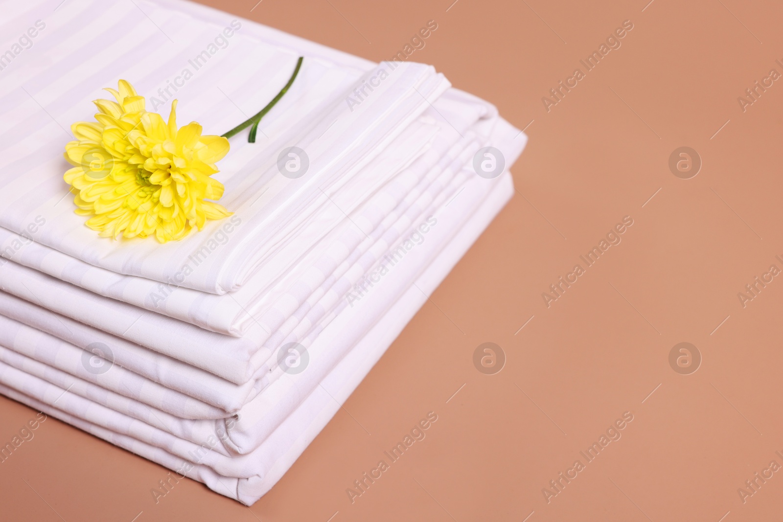 Photo of Stack of clean bed linens and beautiful flower on beige background, closeup. Space for text