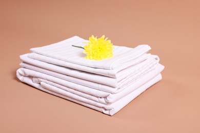 Photo of Stack of clean bed linens and beautiful flower on beige background