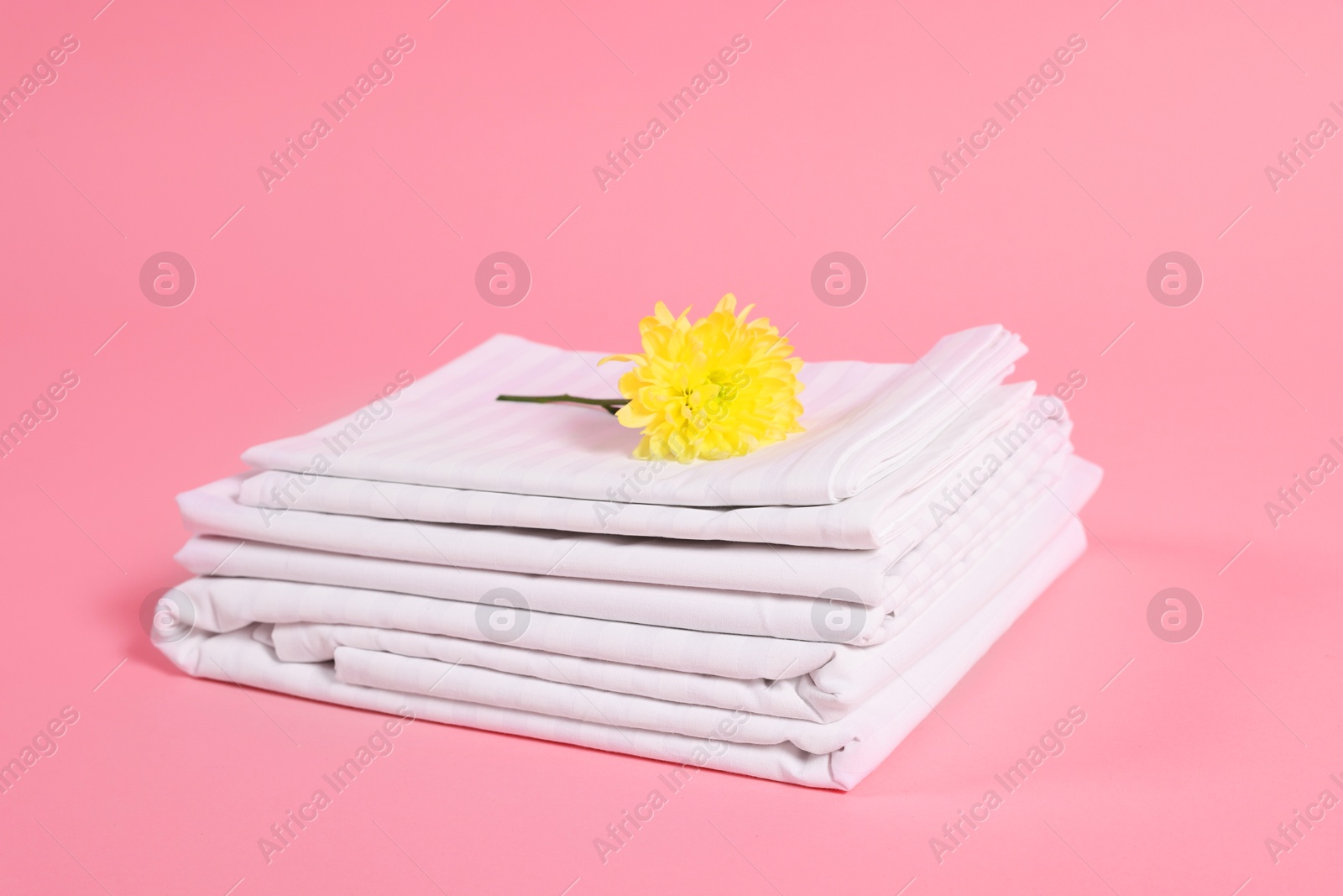 Photo of Stack of clean bed linens and beautiful flower on pink background