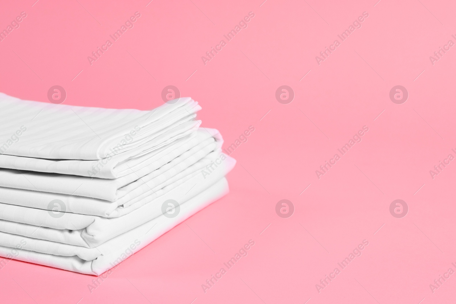 Photo of Stack of clean bed linens on pink background, space for text