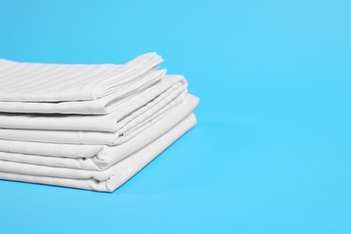 Photo of Stack of clean bed linens on light blue background, closeup. Space for text