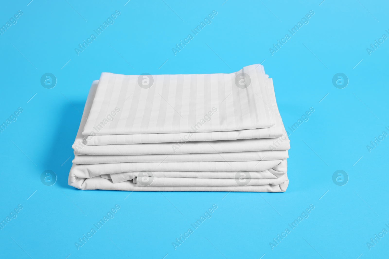 Photo of Stack of clean bed linens on light blue background