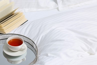 Photo of Tea, book and floral decor on bed with clean linens indoors, space for text