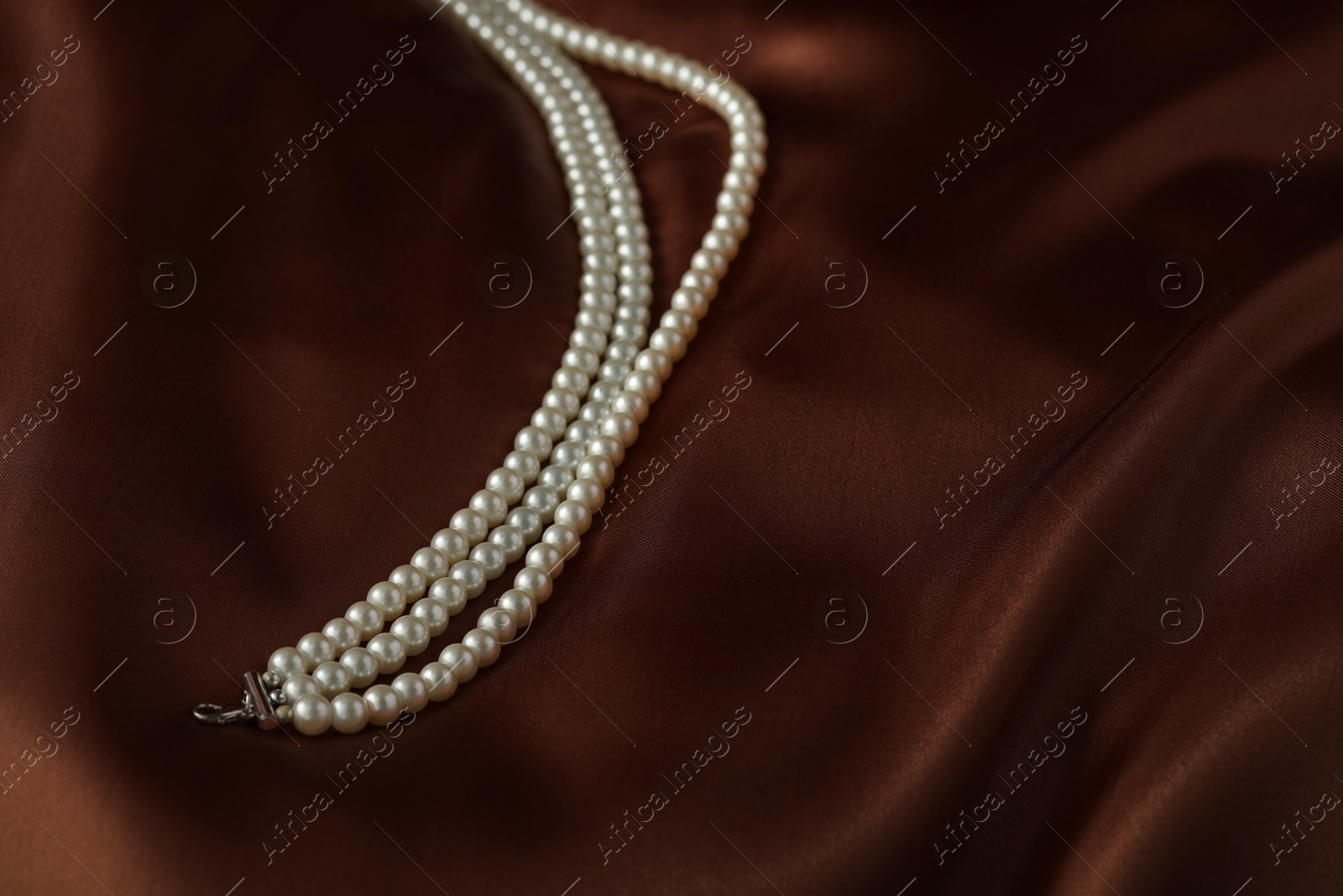 Photo of Beautiful pearl necklace on brown silk, closeup. Space for text