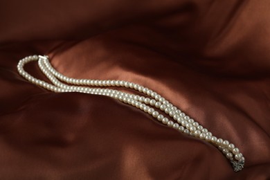 Photo of Beautiful pearl necklace on brown silk, closeup