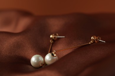 Photo of Beautiful pearl earrings on brown silk, closeup. Space for text