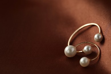 Photo of Beautiful pearl earrings on brown silk, closeup. Space for text