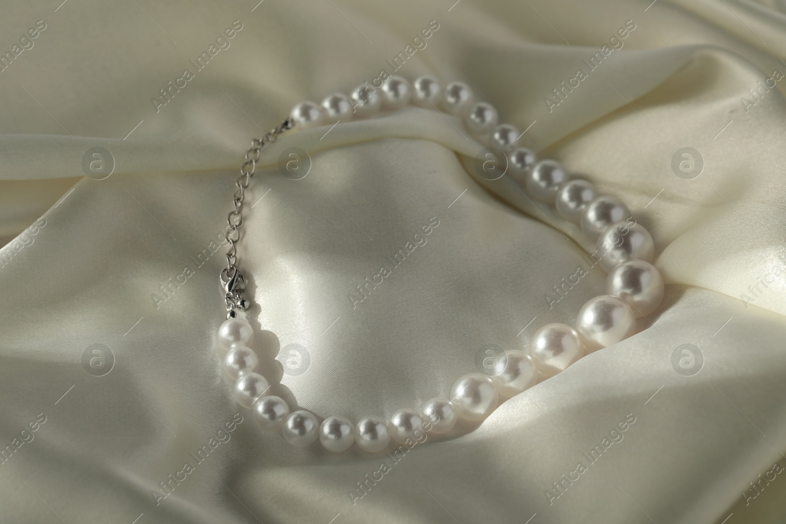 Photo of Beautiful pearl necklace on white silk, closeup