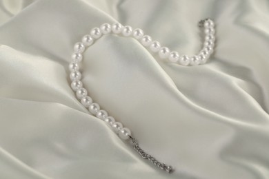 Photo of Beautiful pearl necklace on white silk, closeup