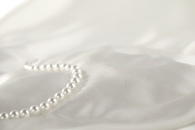 Photo of Beautiful pearl necklace on white silk, closeup. Space for text