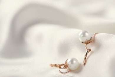 Photo of Beautiful pearl earrings on white silk, closeup. Space for text