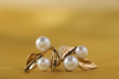 Photo of Beautiful pearl earrings on golden silk, closeup. Space for text