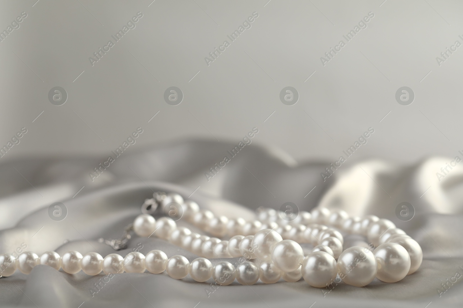 Photo of Beautiful pearl necklace on white silk, closeup. Space for text