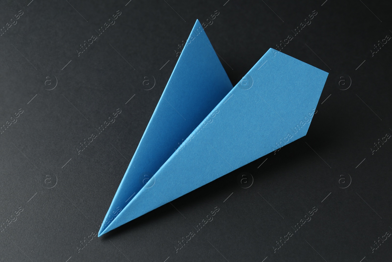 Photo of One handmade light blue paper plane on black background, closeup