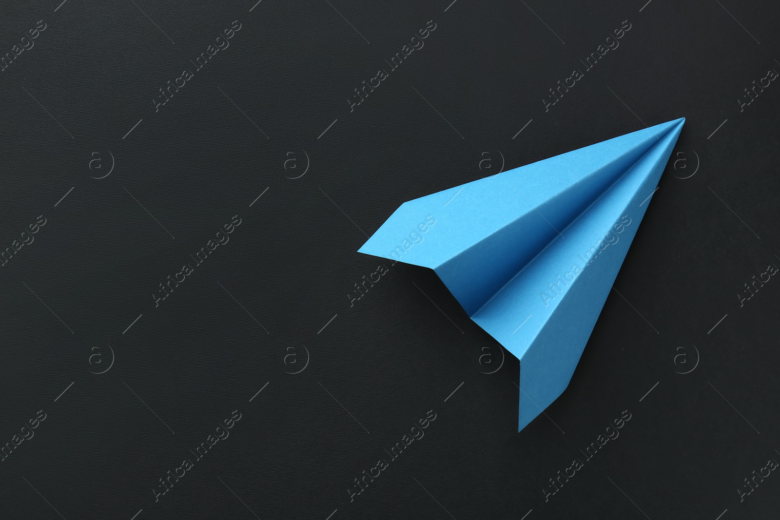 Photo of One handmade light blue paper plane on black background, top view. Space for text