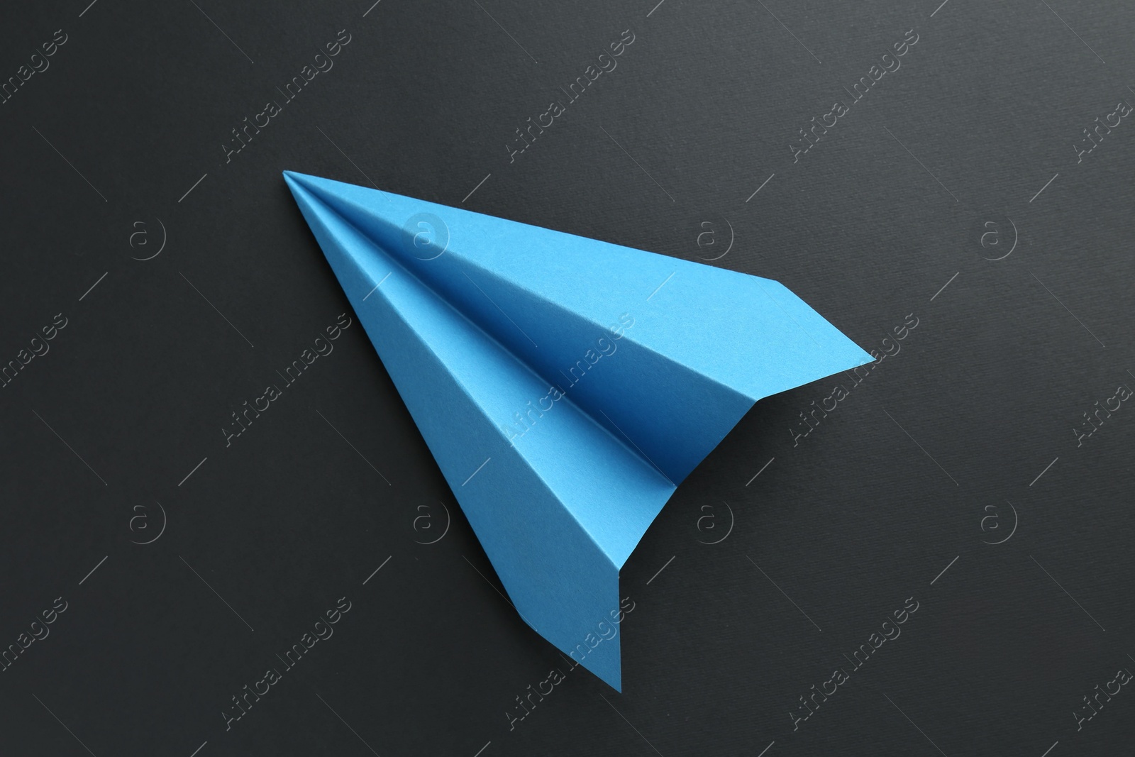 Photo of One handmade light blue paper plane on black background, top view