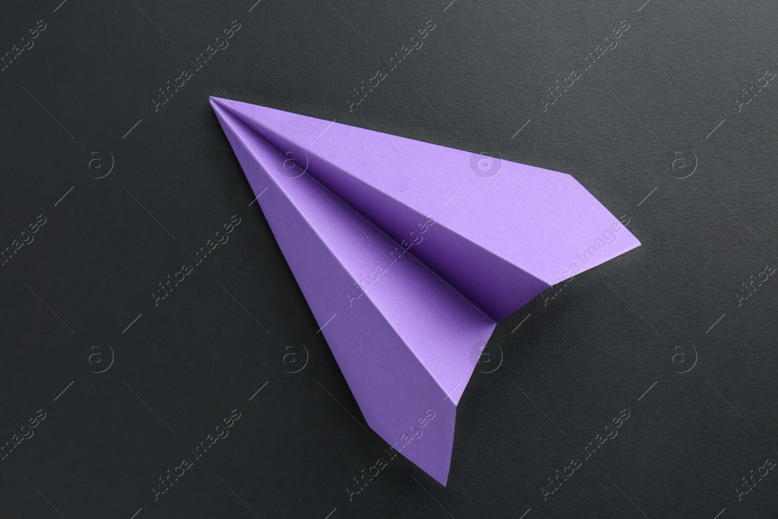 Photo of One handmade violet paper plane on black background, top view