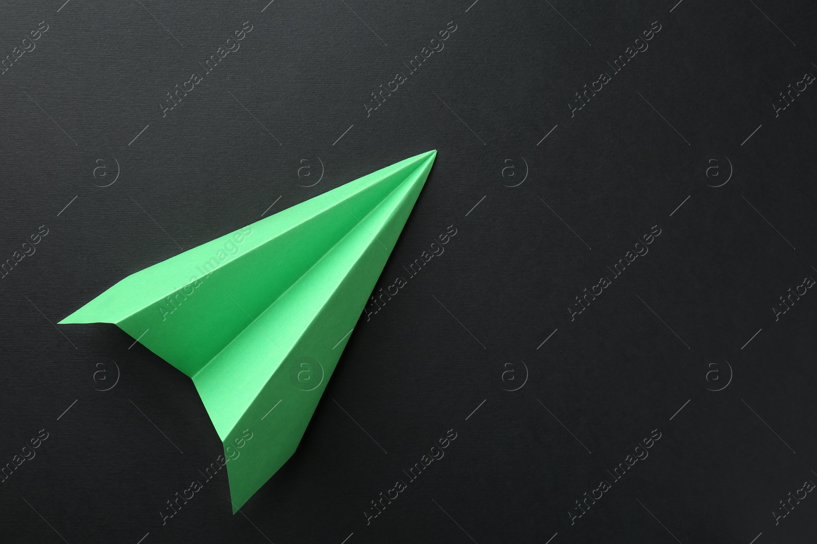 Photo of One handmade green paper plane on black background, top view. Space for text