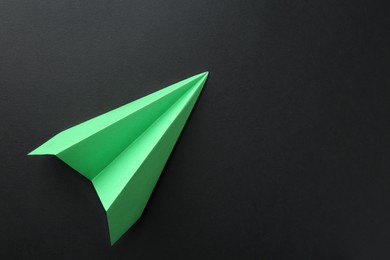 Photo of One handmade green paper plane on black background, top view. Space for text