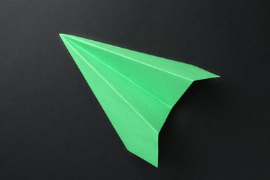 Photo of One handmade green paper plane on black background, top view