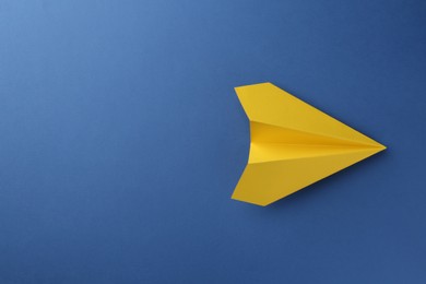 Photo of One handmade yellow paper plane on blue background, top view. Space for text