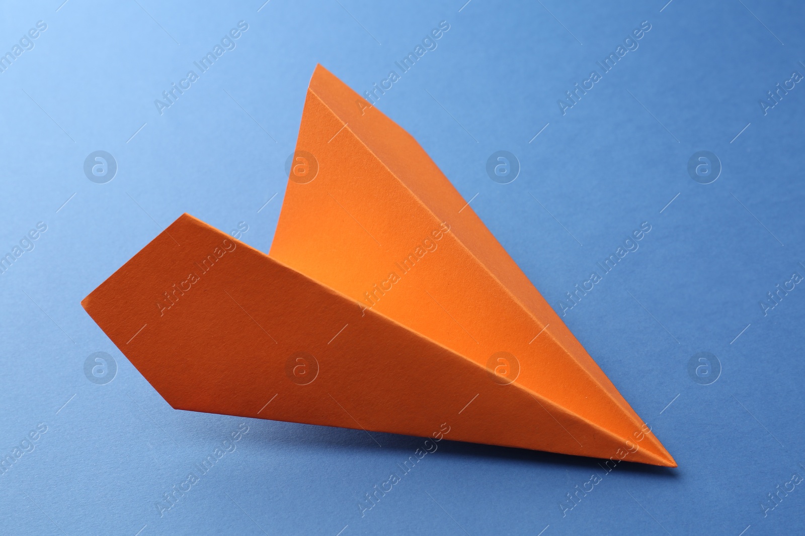 Photo of One handmade orange paper plane on blue background, closeup