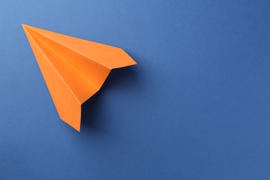 Photo of One handmade orange paper plane on blue background, top view. Space for text