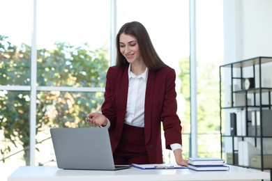 Photo of Portrait of young woman with laptop wearing stylish suit at white table indoors