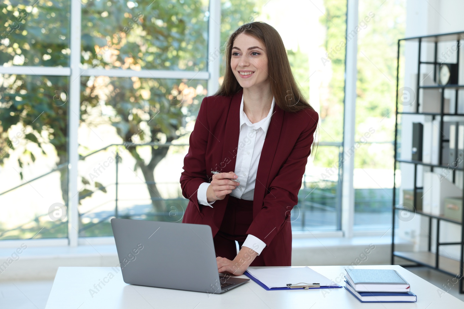 Photo of Portrait of young woman with laptop wearing stylish suit at white table indoors