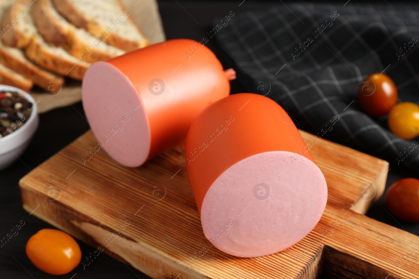 Photo of Tasty boiled sausage, tomatoes, spices and bread on black table, closeup