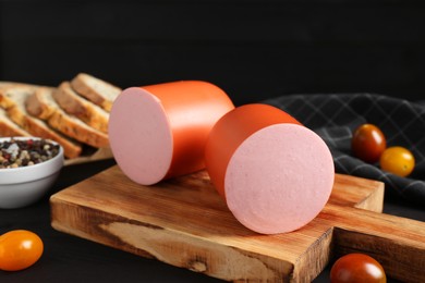 Photo of Tasty boiled sausage, tomatoes, spices and bread on black table, closeup