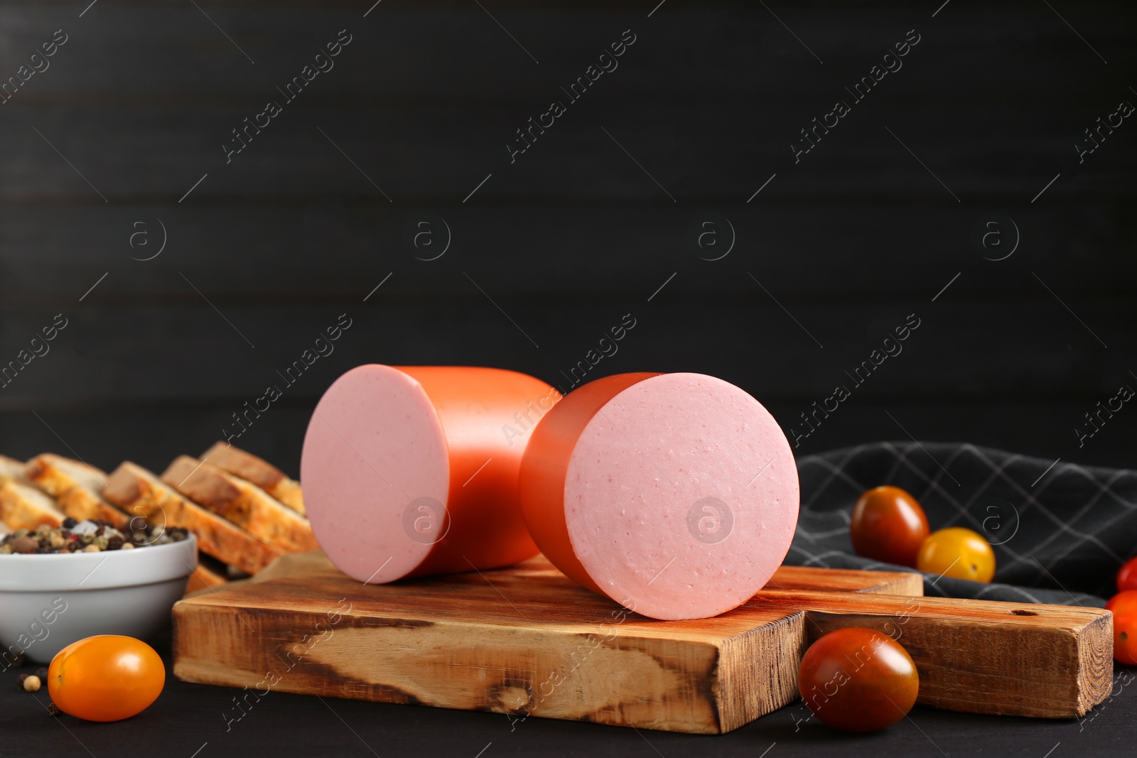 Photo of Tasty boiled sausage, tomatoes, spices and bread on black wooden table