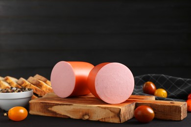 Photo of Tasty boiled sausage, tomatoes, spices and bread on black wooden table