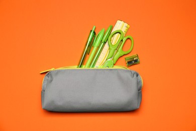 Photo of Pencil case and different stationery on orange background, flat lay