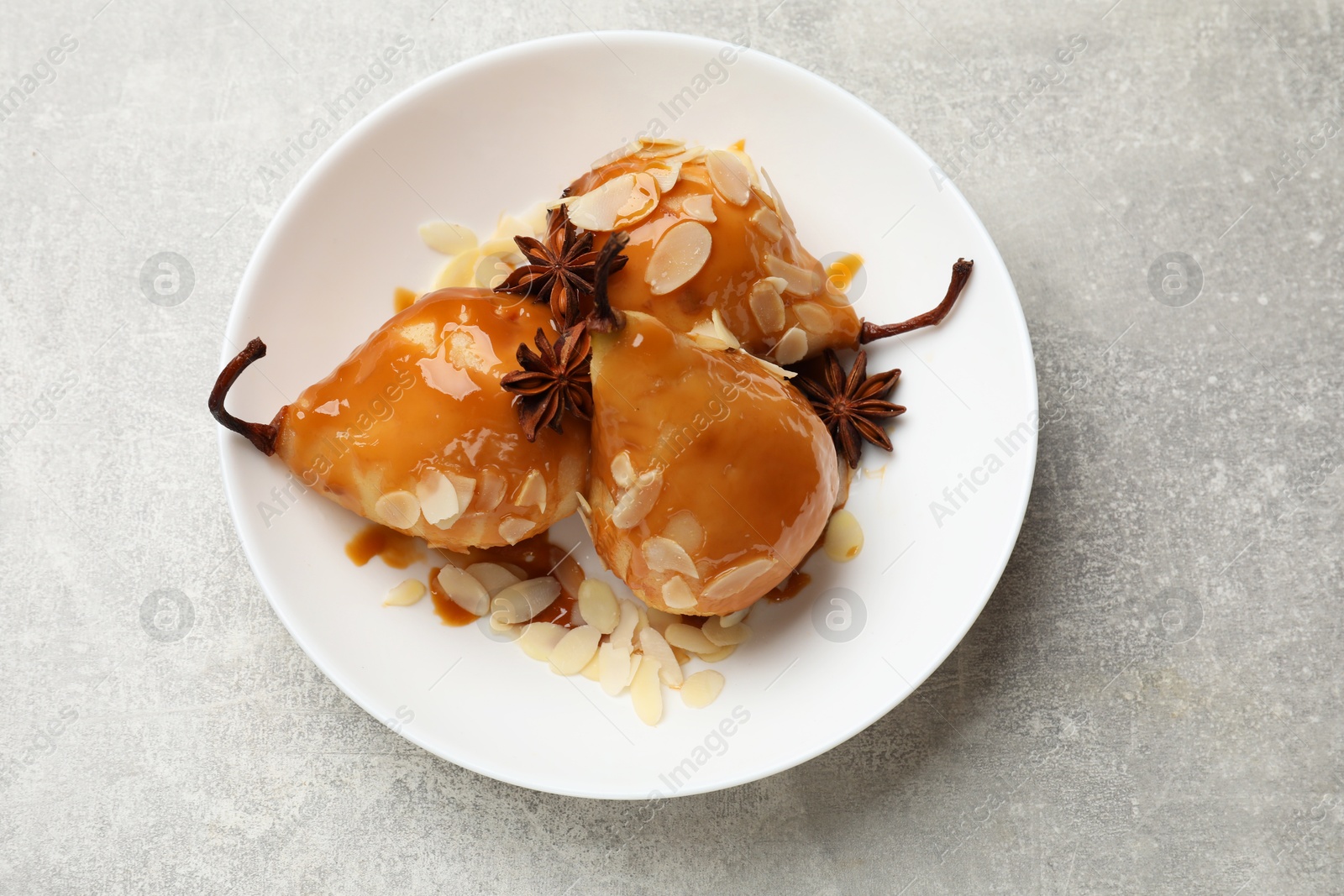 Photo of Delicious pears with caramel sauce, almond flakes and anise stars on grey table, top view